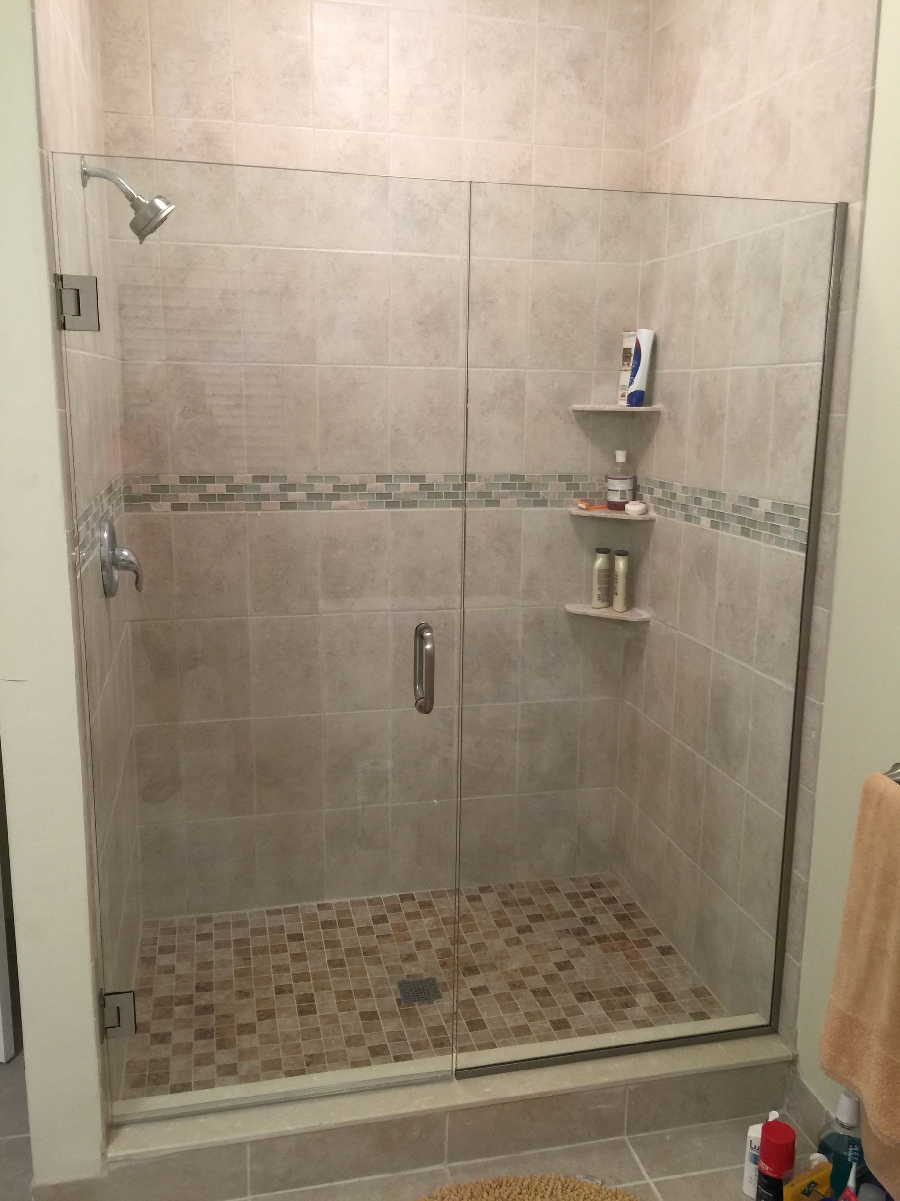 Shower stall with glass doors, beige tile, pebble floor, and built-in shelves holding toiletries.