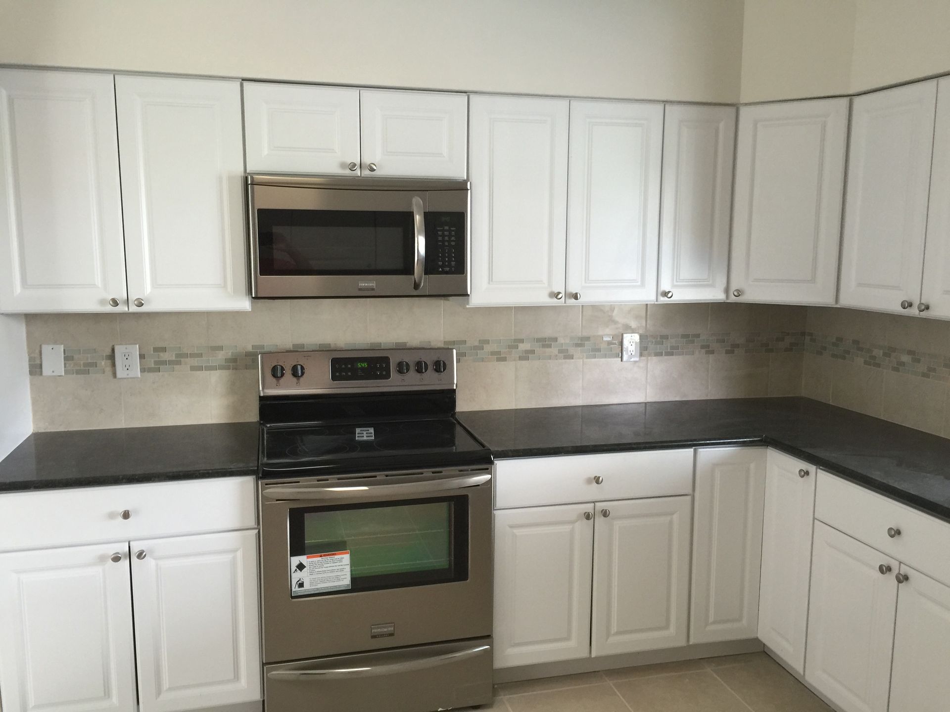 White kitchen cabinets with stainless steel appliances and black countertops.