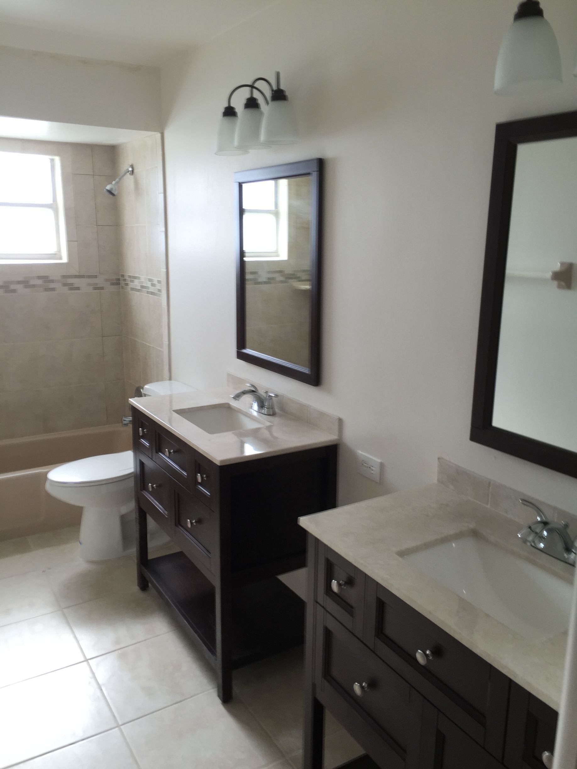Bathroom with two dark wood vanities, each with a mirror and light fixture.