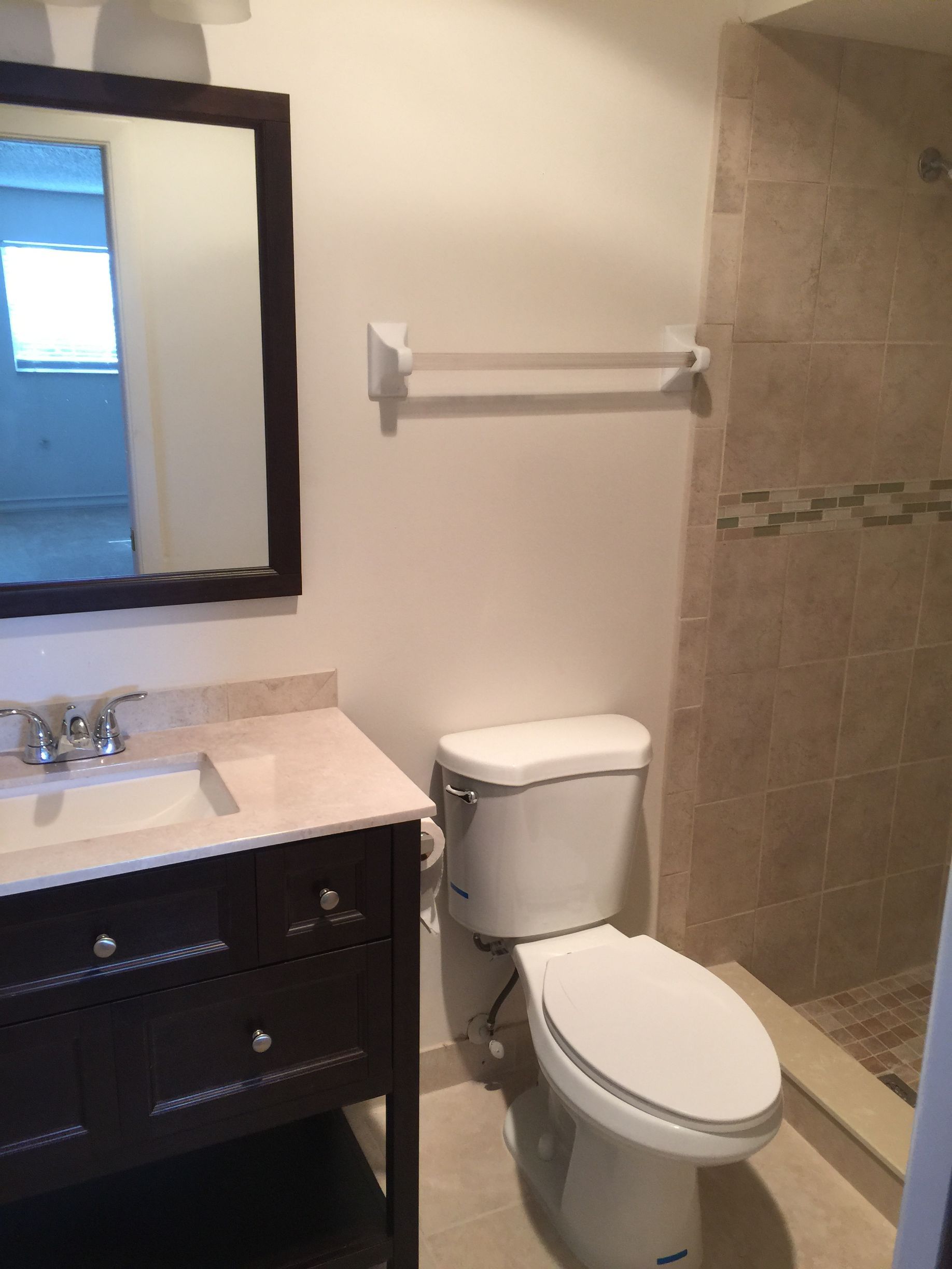 Bathroom with dark vanity, toilet, and tiled shower. A mirror hangs over the sink.