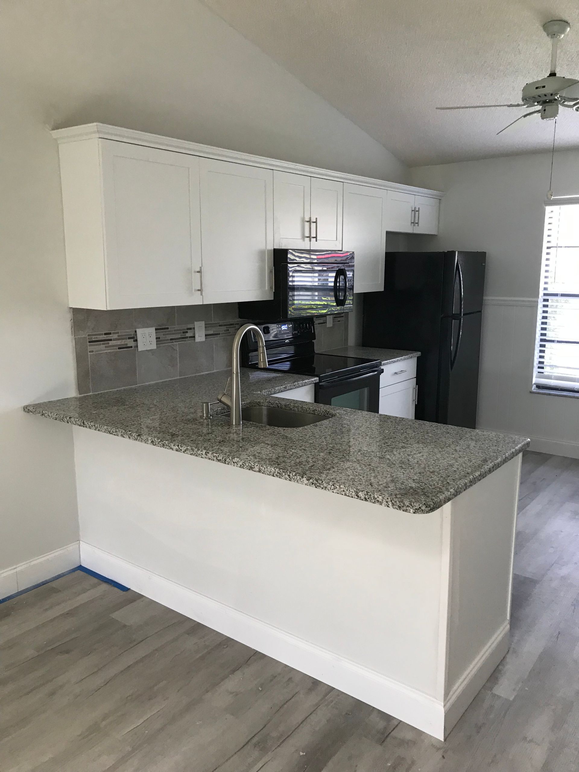 White kitchen with granite countertop island, black appliances, and gray flooring.