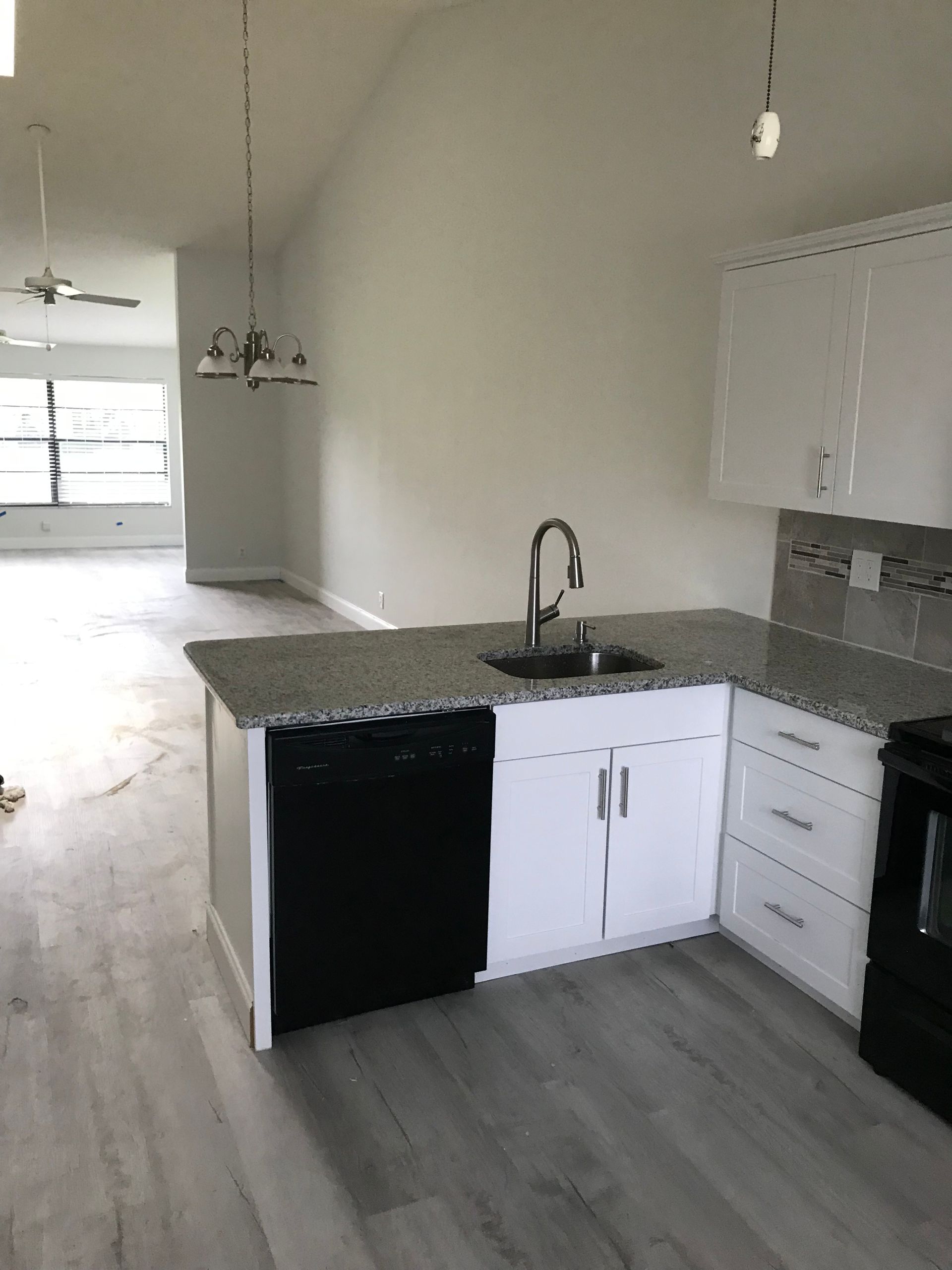 Kitchen with gray countertops, white cabinets, black dishwasher, and gray flooring.