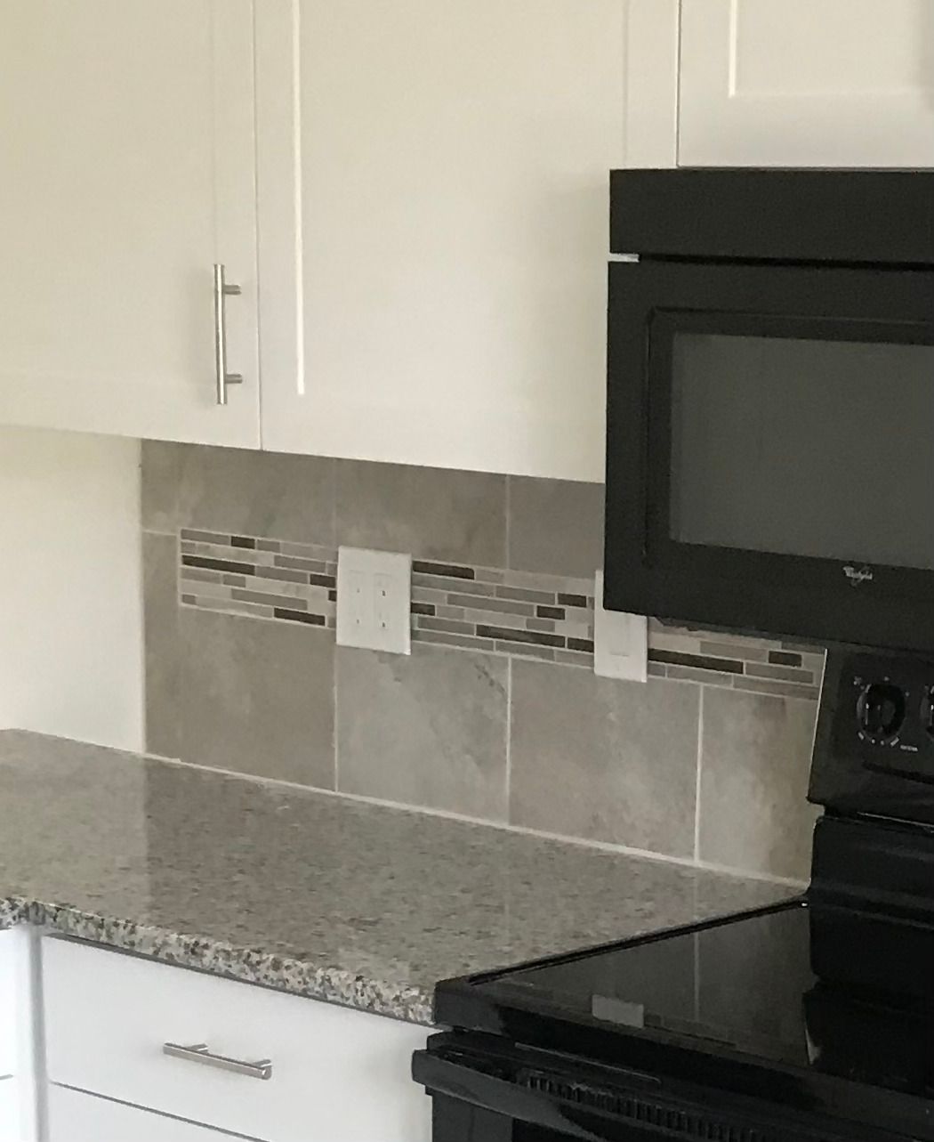Kitchen with white cabinets, gray backsplash, and black appliances.