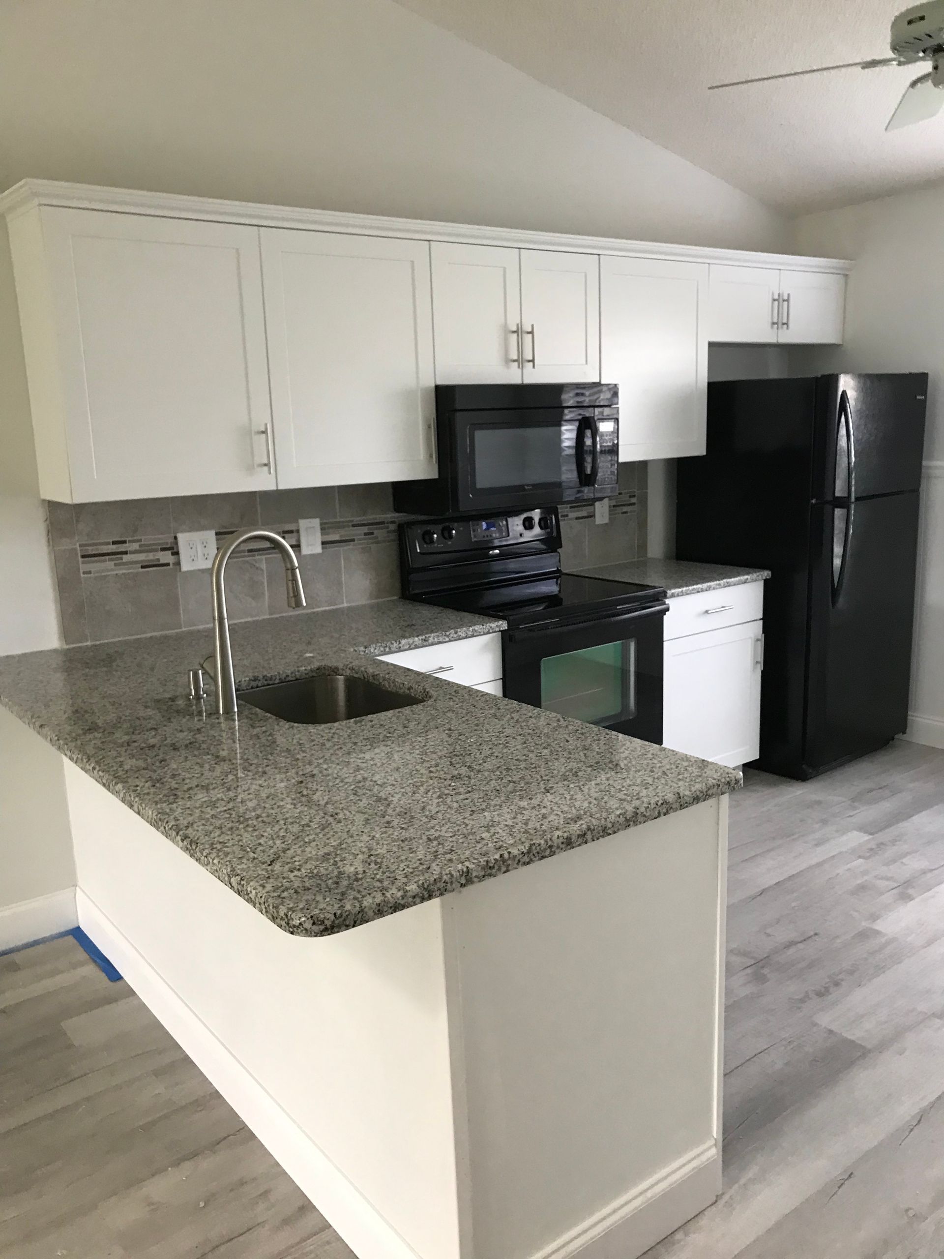 Kitchen with white cabinets, gray granite countertop, black appliances, and a small island.