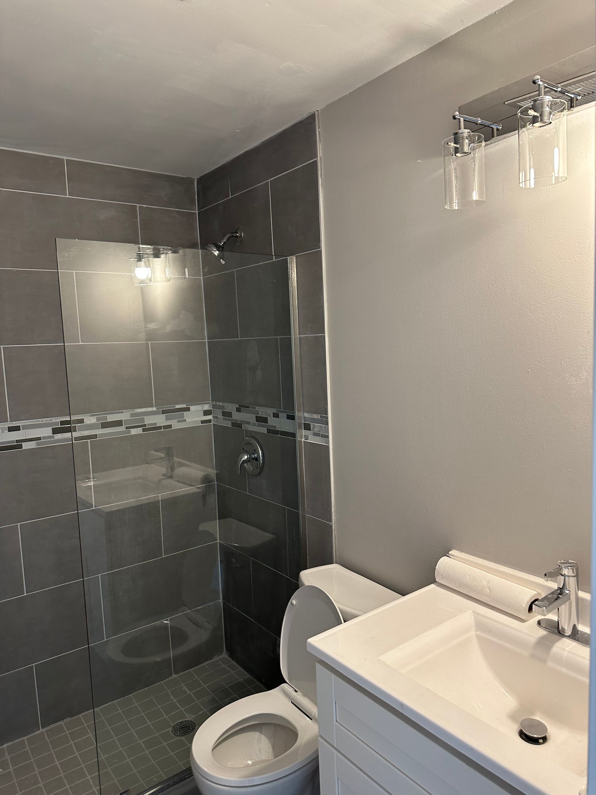 Bathroom with gray tile shower, white toilet and vanity, and silver fixtures.