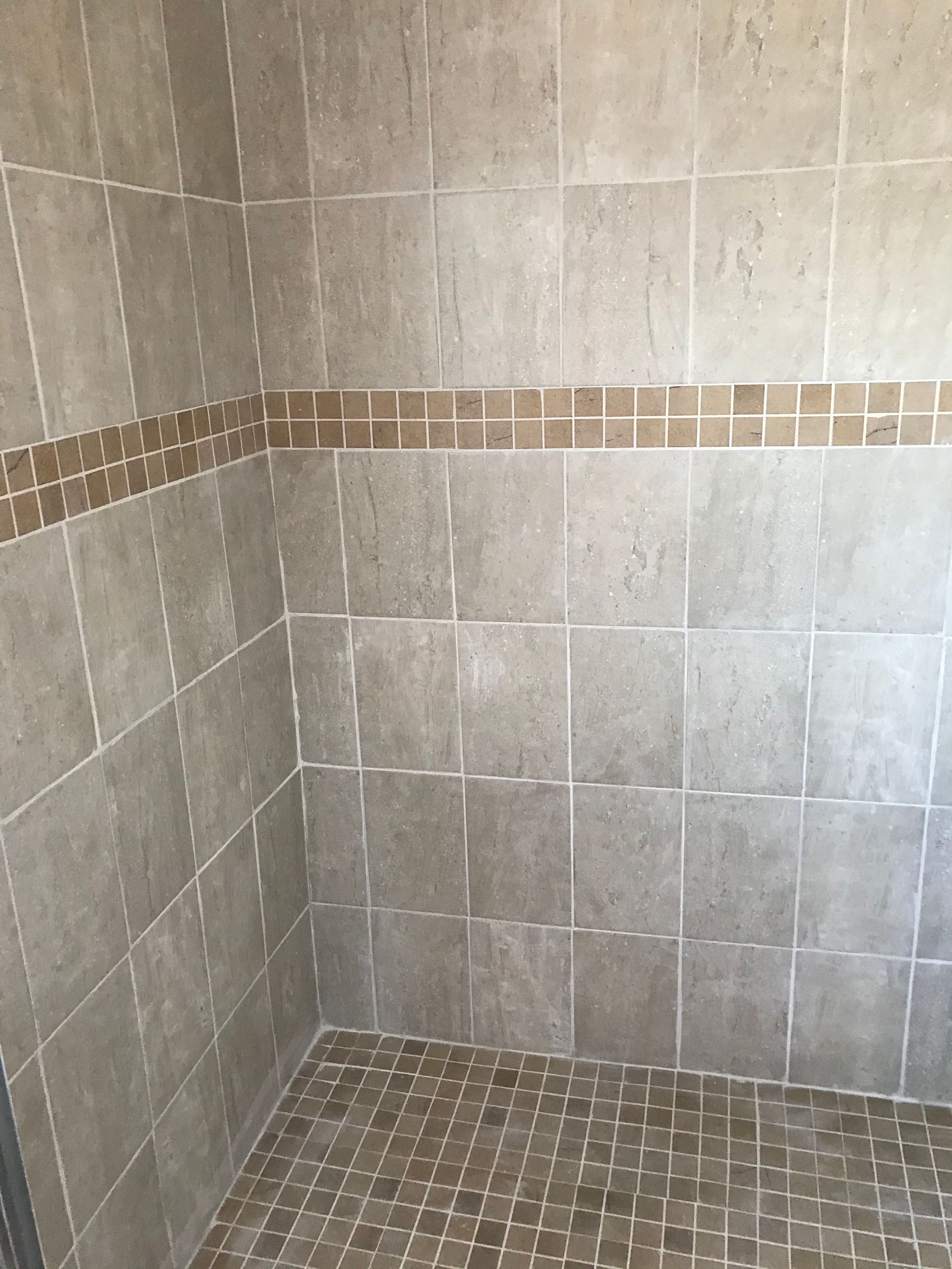 Beige tiled shower with a brown mosaic border and floor.