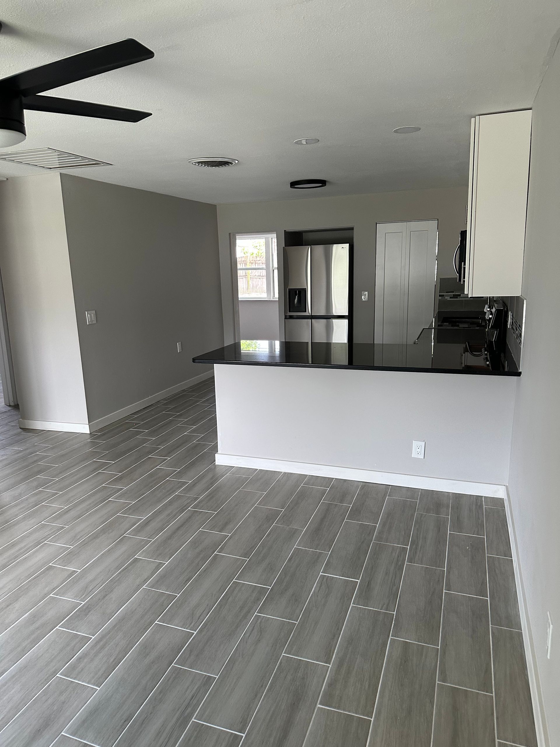 Open kitchen and living space with gray tiled floors, gray walls, and black countertops.