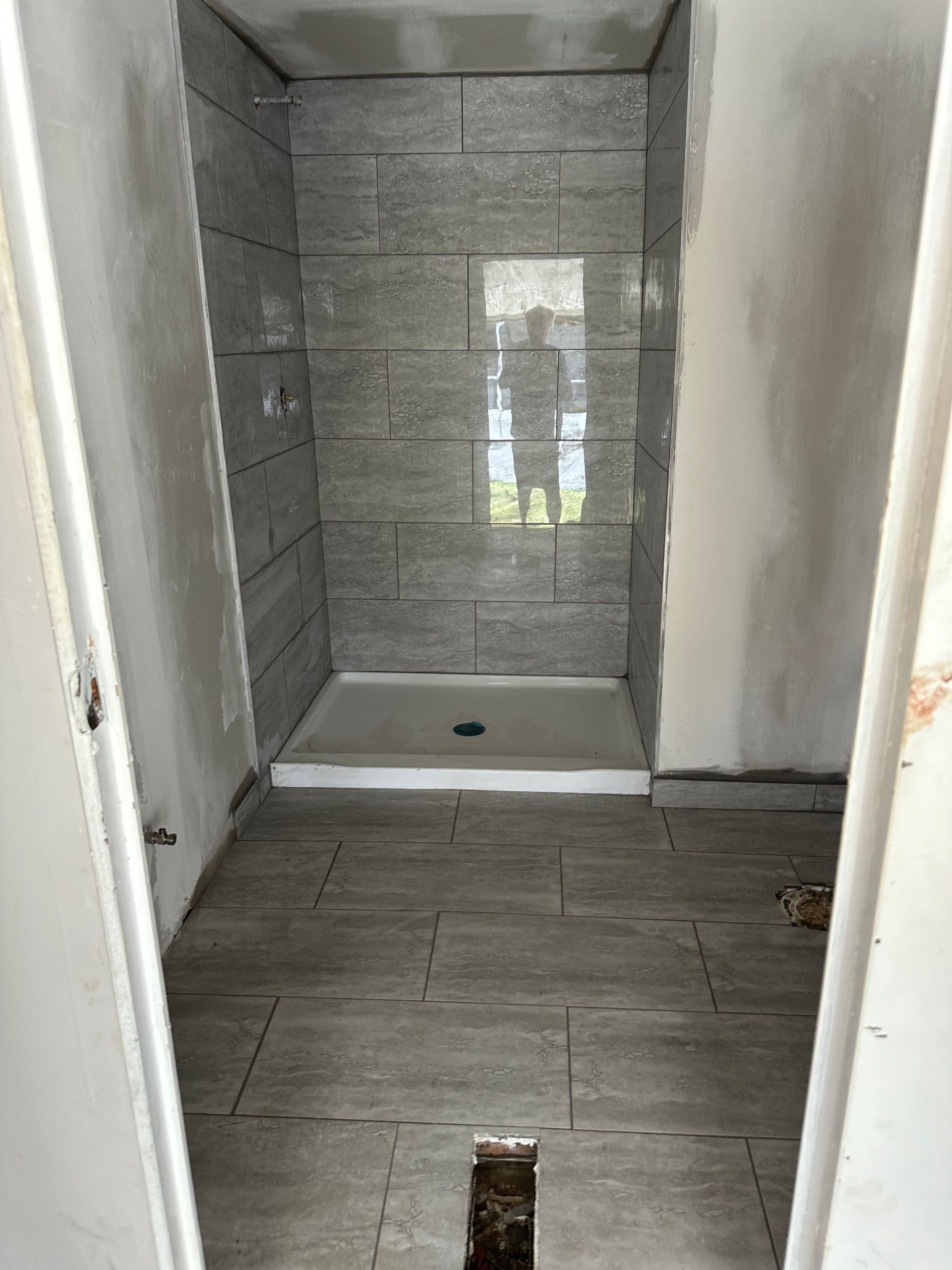 Shower stall under construction, gray tiled walls and floor, white base, unfinished walls surrounding.