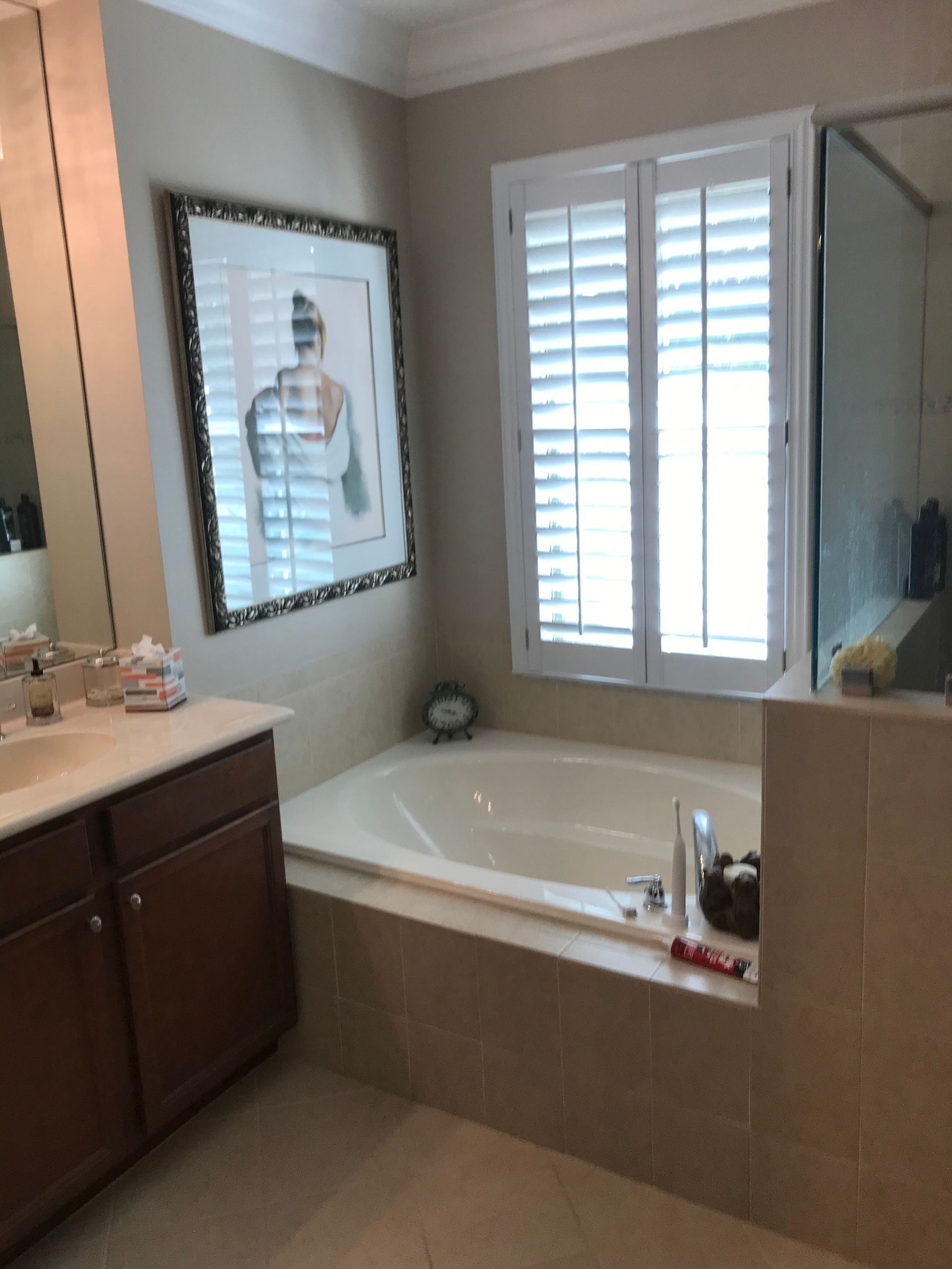 Bathroom with a bathtub, sink, window with shutters, and artwork.