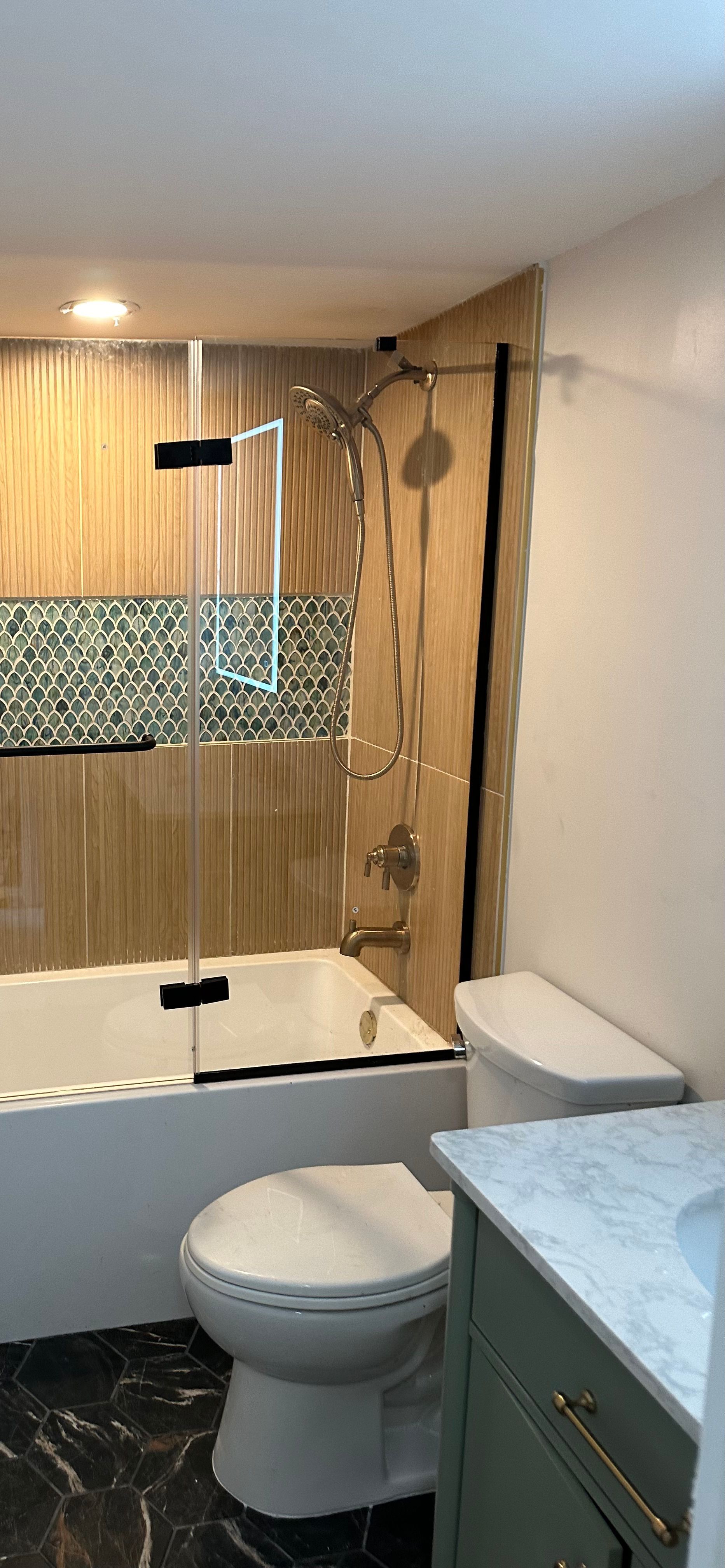 Bathroom with a bathtub, toilet, and shower fixtures. The walls are tiled, and the floor has a marble pattern.