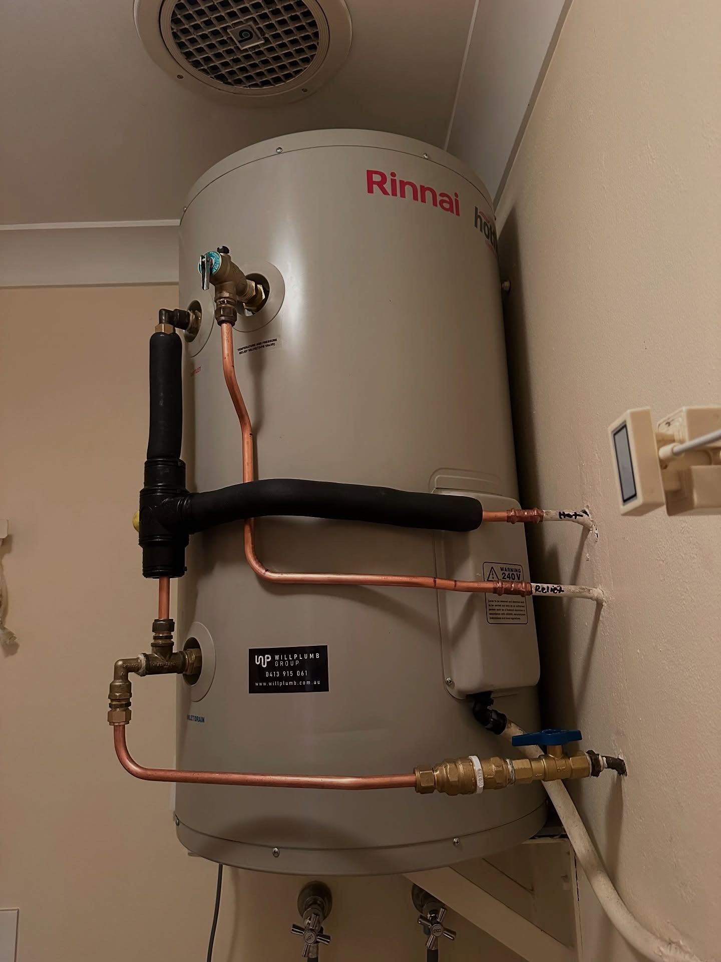 A Rinnai water heater mounted on a beige wall with visible copper piping and insulation inside a room.