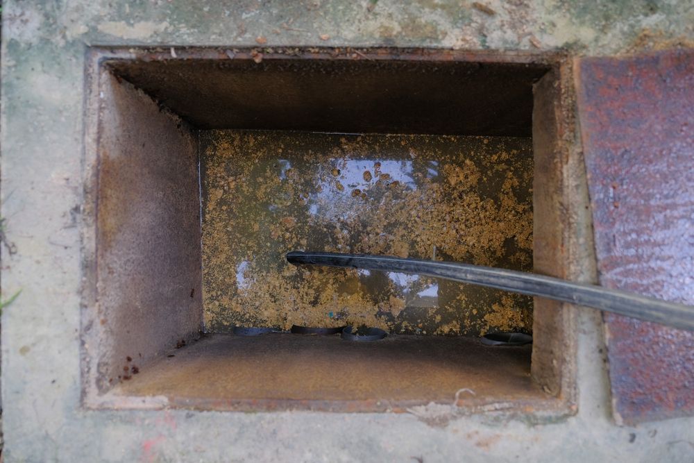 A rectangular concrete utility pit containing murky water and a black cable extending from the side into the water.