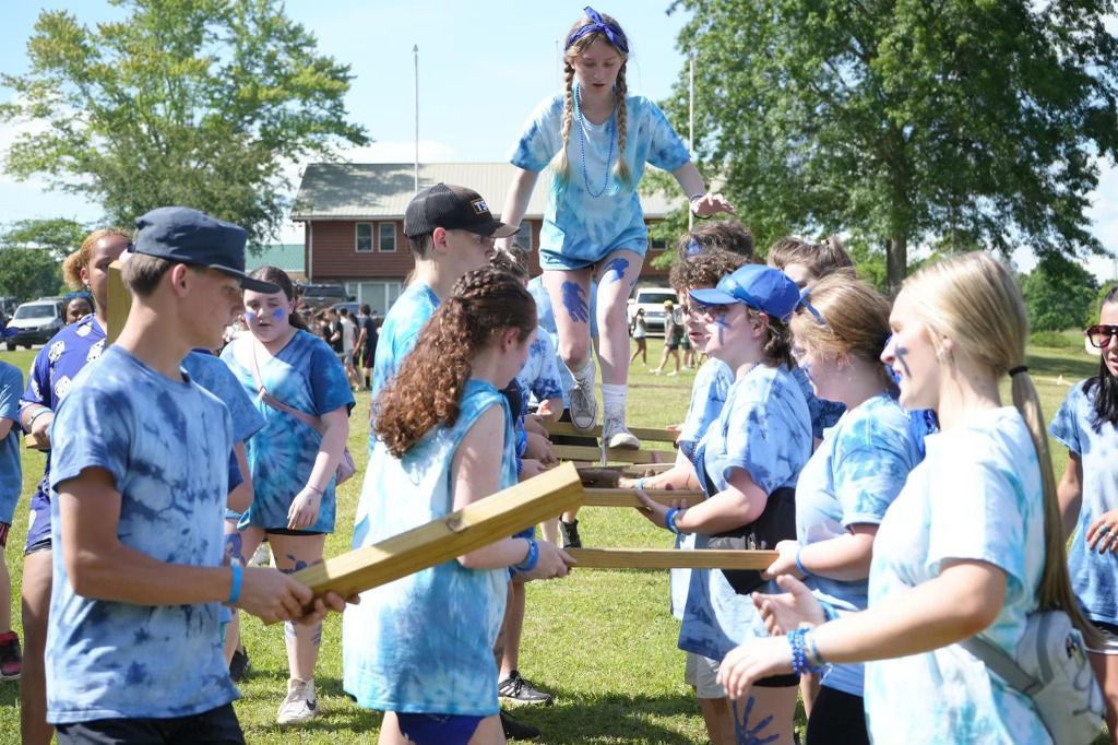 A group of people in blue shirts are standing in a field holding wooden sticks.