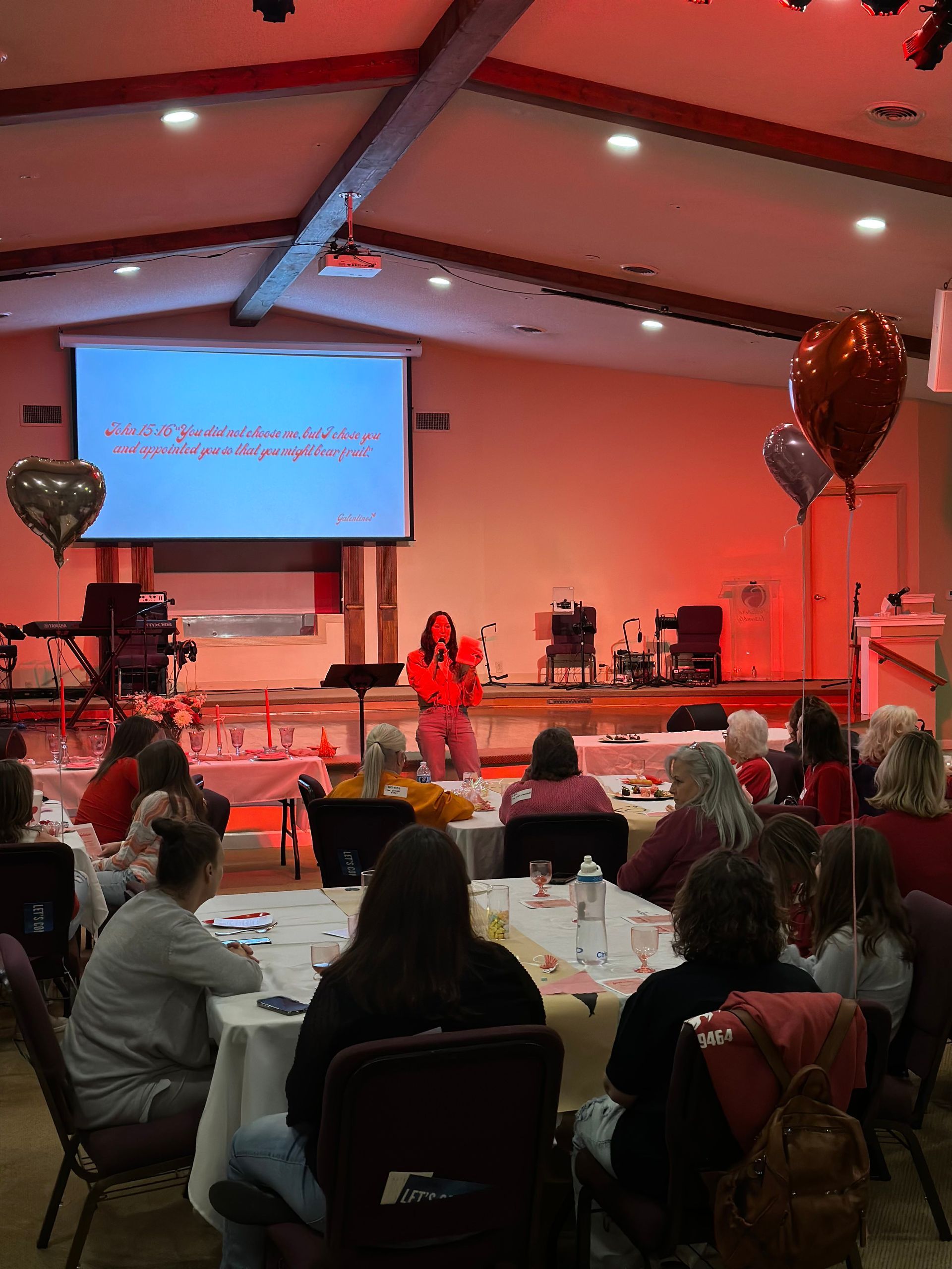 A group of people are sitting at tables in front of a large screen.