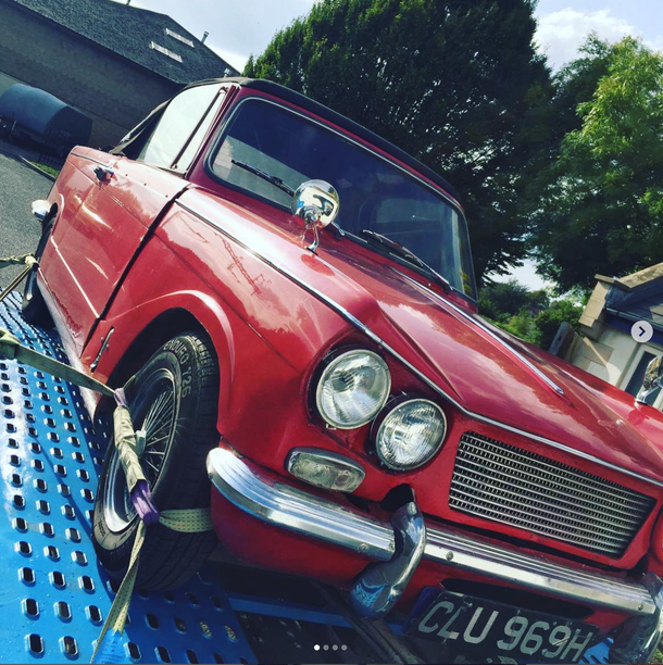 Red vintage car on a blue tow truck, front view, outdoors on a sunny day.