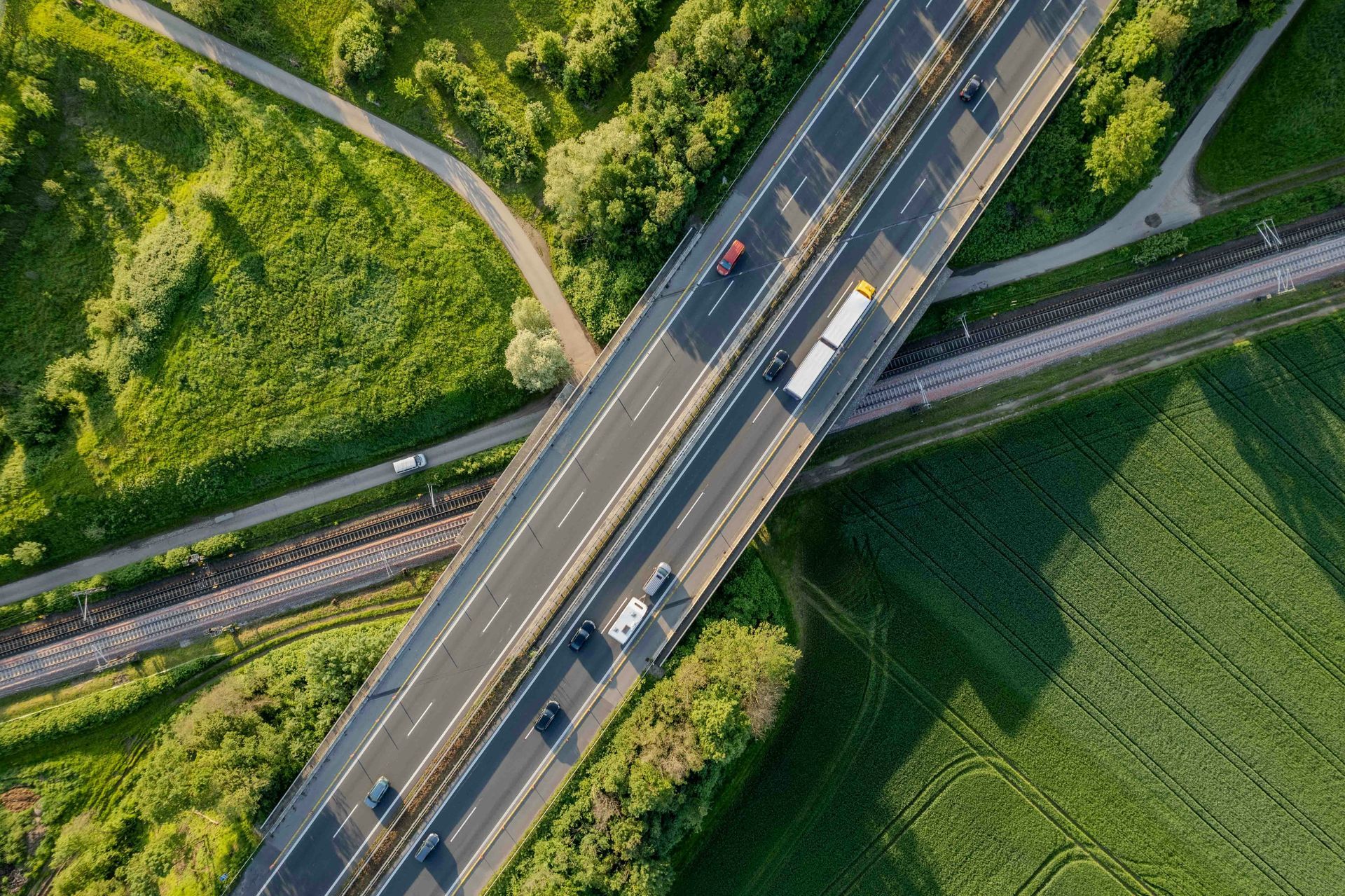 Aerial view of a highway overpass spanning train tracks and fields, with a few vehicles.