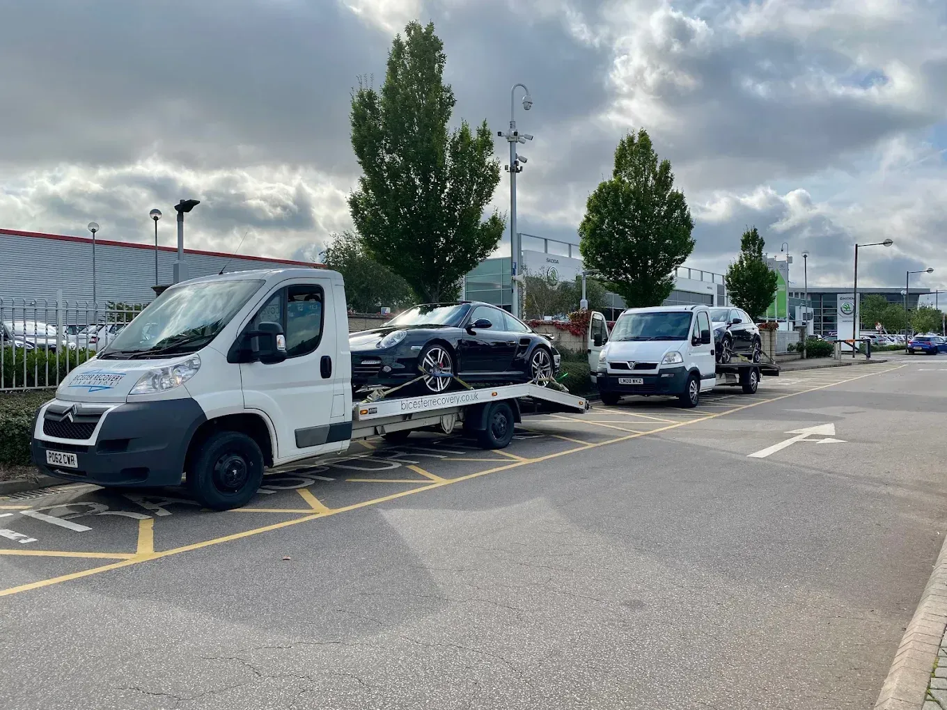 Two tow trucks, one loaded with a black car, parked on a paved lot.