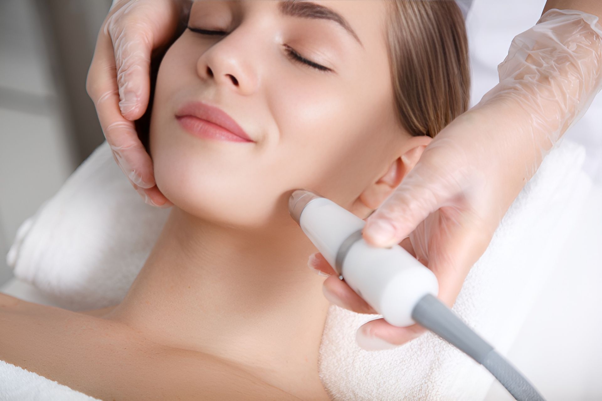 A Woman is Getting a Facial Treatment With a Roller on Her Face — Nurose Aesthetics in Nundah, QLD