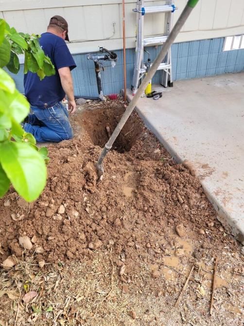 Man digging a hole next to a concrete sidewalk, near a building.