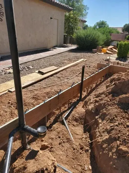 Construction site: trench with wooden forms and plumbing pipes in front of a house.