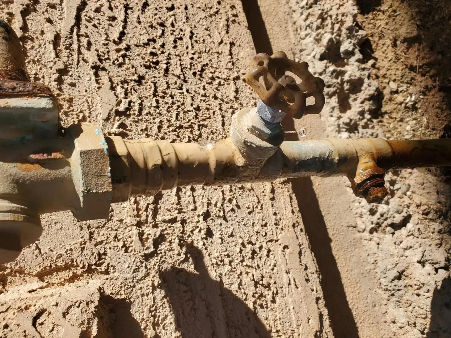 Rusty water pipe with valve against textured tan wall.