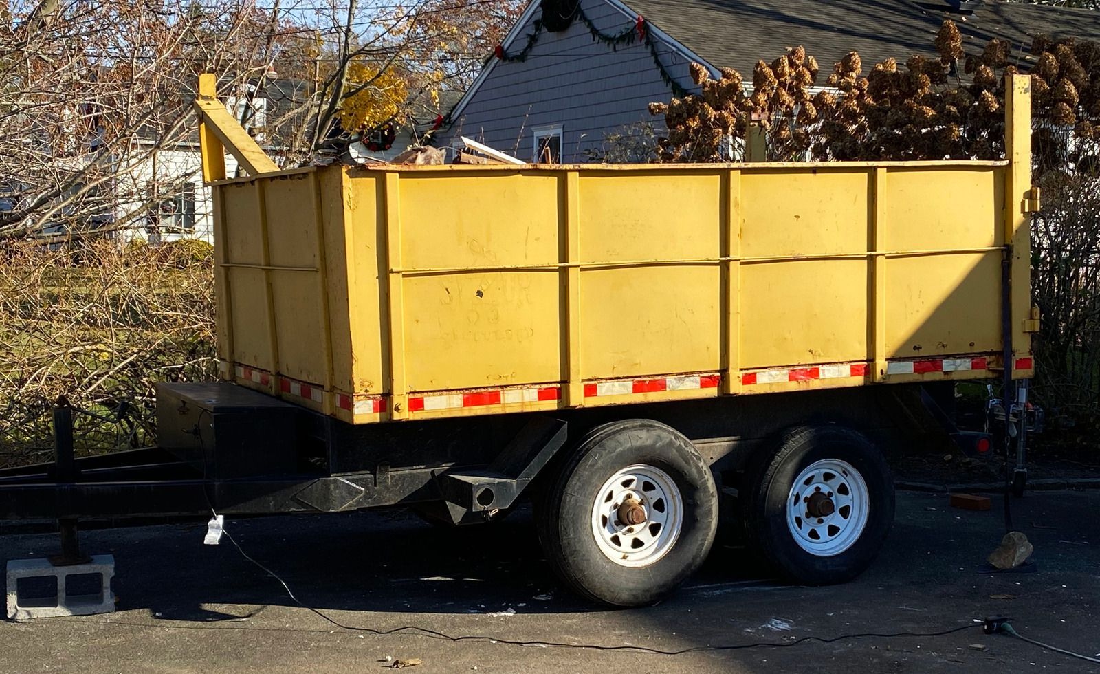 Yellow trailer loaded with debris on a street, parked near a house.