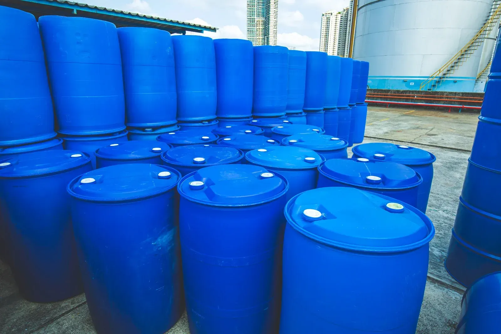 Blue plastic barrels stacked outdoors near storage tanks.