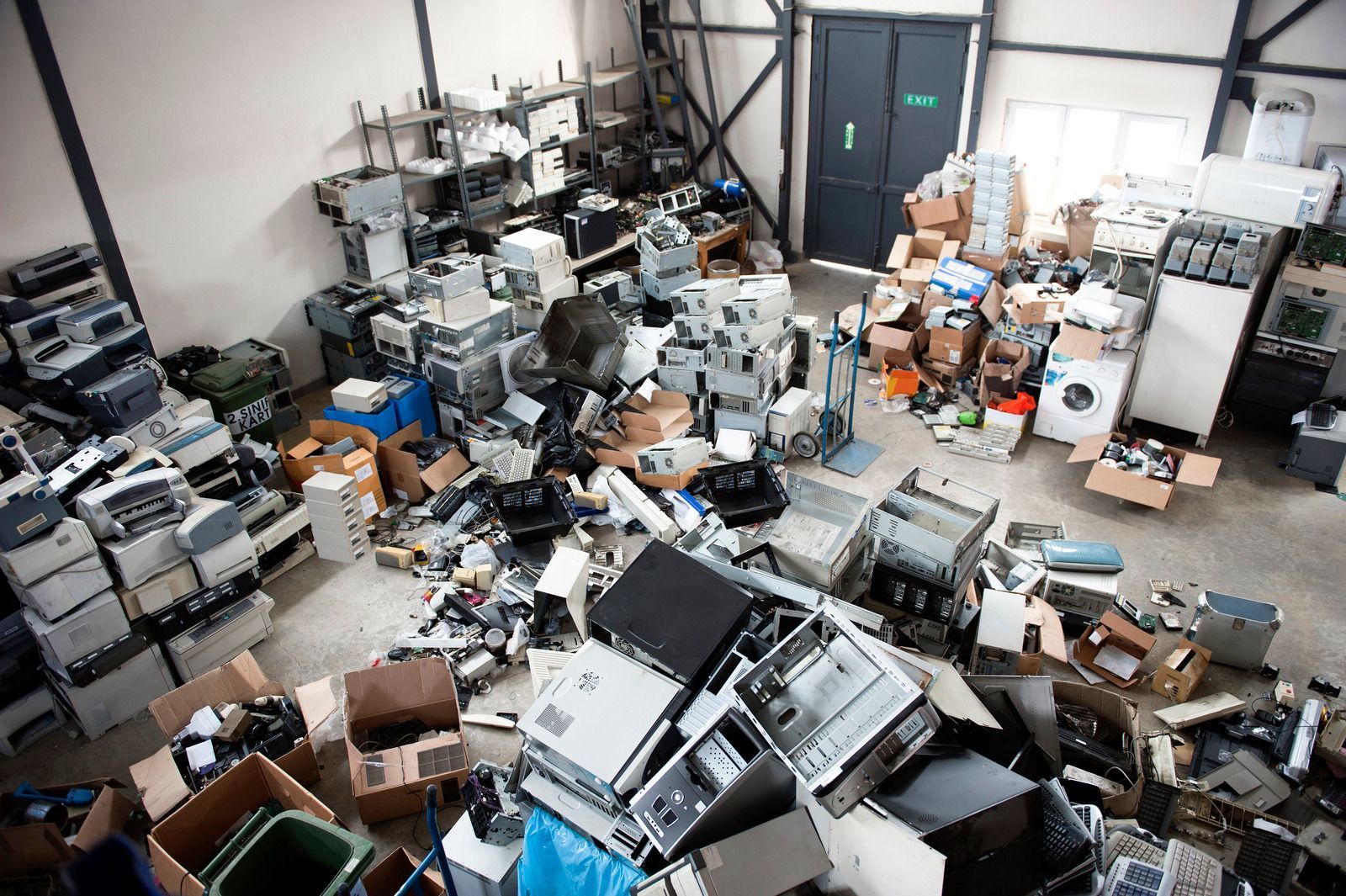 Hands sorting through a box of electronic waste, including a phone, cables, and keyboards.