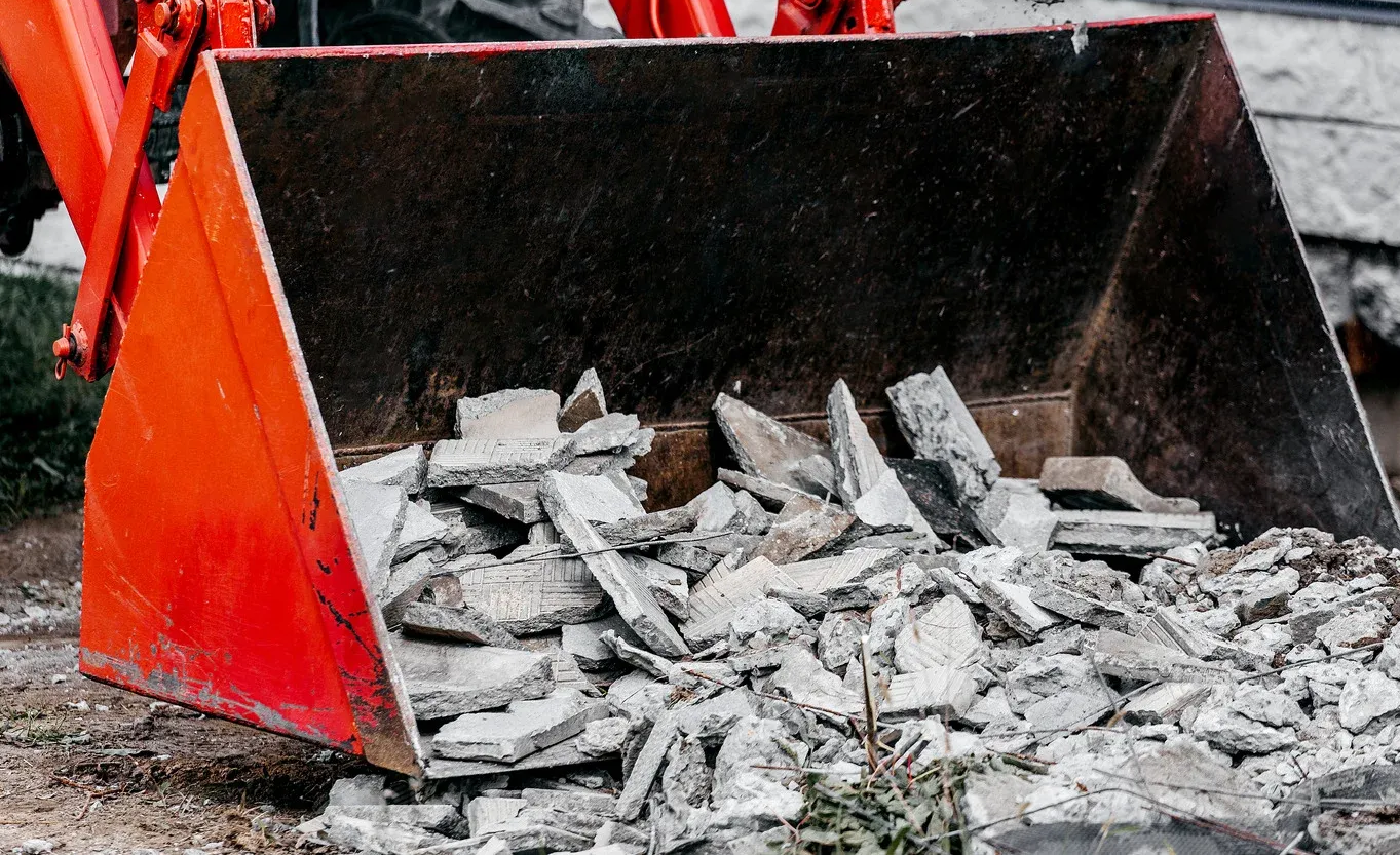 An excavator demolishes a concrete structure, with a pile of debris in a construction zone.