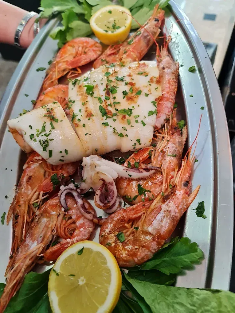 Piatto di frutti di mare grigliati con fette di limone e guarnizione di prezzemolo su un vassoio d'argento.