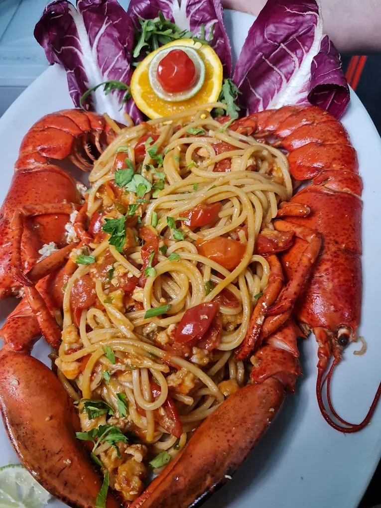 Piatto di pasta all'astice con chele rosse, spaghetti al pomodoro e lattuga viola su un piatto bianco.