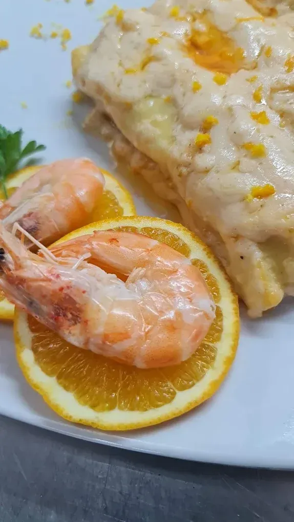 Gamberetti e fette di limone accanto a un filetto di pesce cremoso su un piatto bianco.
