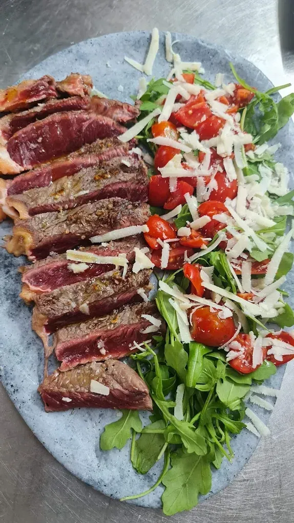 Fettine di bistecca grigliata con verdure, pomodorini e formaggio grattugiato su un piatto grigio.