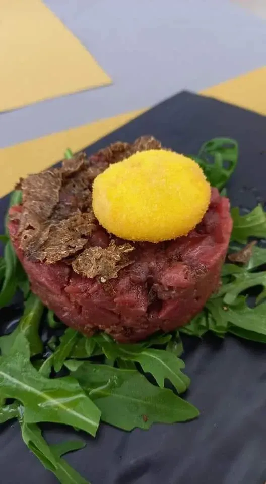 Piatto gourmet di tartare di manzo crudo con tuorlo d'uovo giallo brillante su rucola, impiattato su ardesia nera.