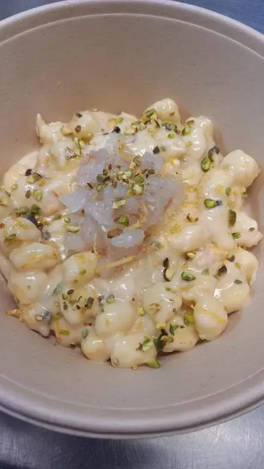 Pasta cremosa in una ciotola condita con formaggio grattugiato e pistacchi tritati.