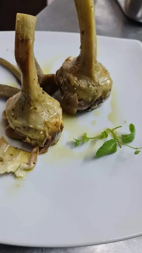 Due costolette di agnello cotte su un piatto bianco con una piccola guarnizione di erbe aromatiche.