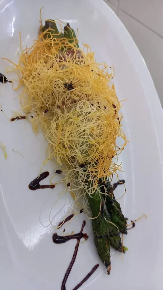 Piatto bianco con asparagi ricoperti di formaggio grattugiato e glassa di aceto balsamico.