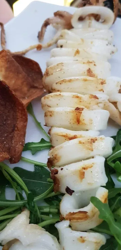 Anelli di calamari grigliati su un letto di verdure con funghi rosolati su un piatto bianco.