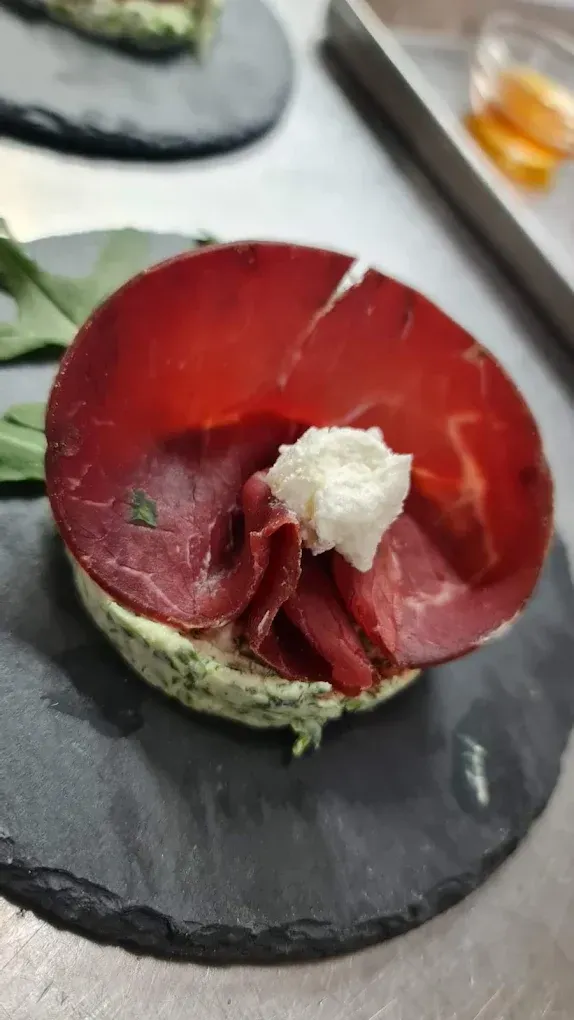 Dessert a forma di fiore rosso con guarnizione bianca su un piatto di ardesia nera.