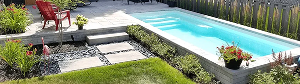 Une piscine rectangulaire aux eaux turquoise est entourée d'aménagements paysagers, avec une chaise rouge visible.