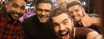 Five smiling men taking a selfie in a bar, one giving a thumbs up.
