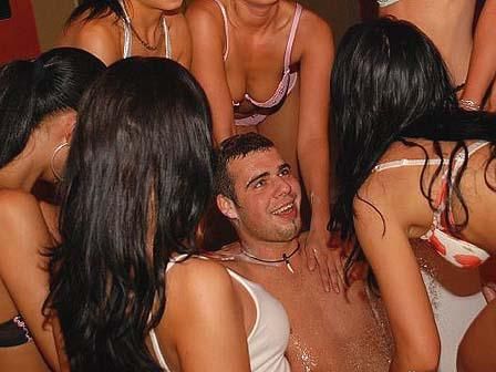 Man surrounded by women in swimsuits; he smiles amid the group, possibly in a hot tub.
