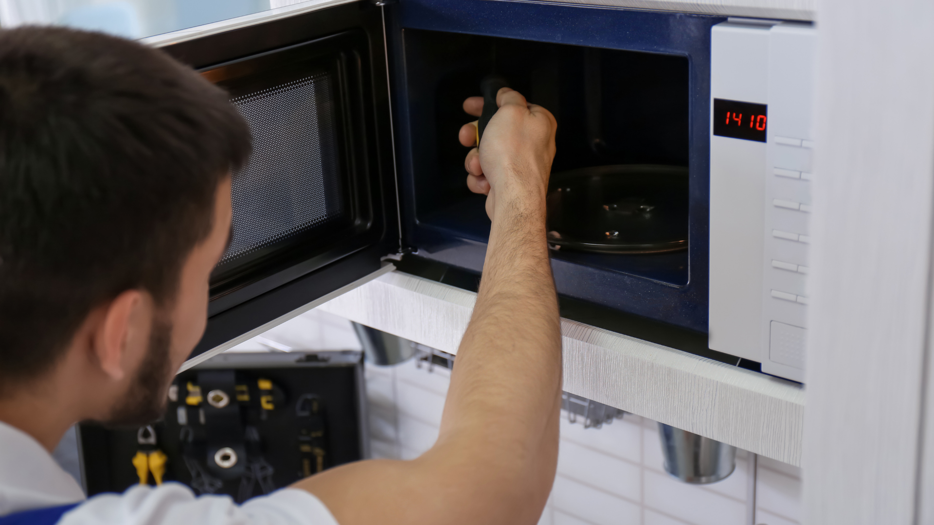 Man reaching into a microwave to retrieve an item, the oven door open. Time display shows 14:30.