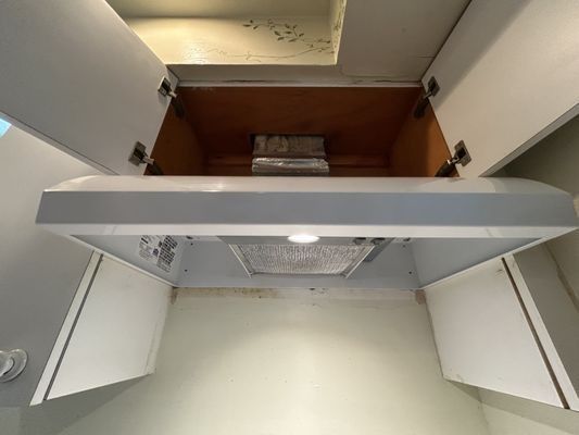 Kitchen range hood with open cabinets. The hood is white, with cabinets and wooden shelving visible above.