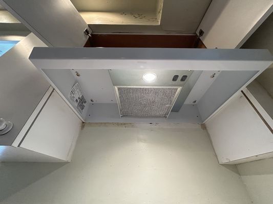A low-angle view inside a kitchen range hood. It is white, with a light and a metal mesh filter. Two white cabinets are on either side.