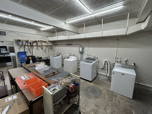 A utility room with several washing machines, a work table with tools, and overhead shelving.
