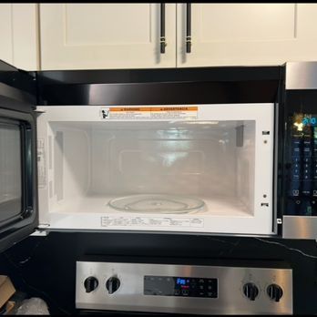 Open microwave above a stove in a white kitchen. The microwave is empty with a glass plate inside. The stove is stainless steel.