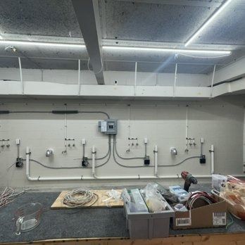 Electrical wiring in a commercial building, with conduit running along the wall and a worker near supplies on a workbench.