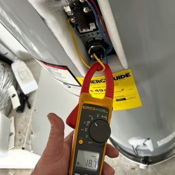A person using a clamp meter to measure the electrical current of a hot water heater. The meter reads 18.7 amps.