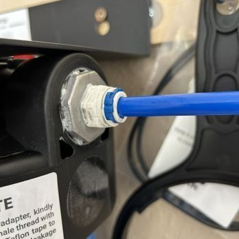 A blue plastic tube connected to a fitting on a black device. The fitting has a white seal.